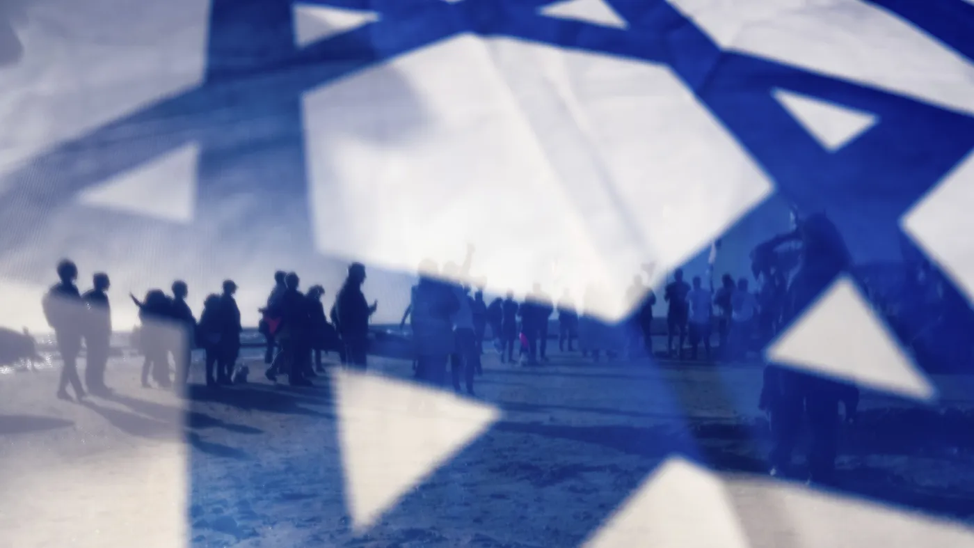 Израильские демонстранты на фоне государственного флага Израиля во время акции протеста против планов правительства премьер-министра Биньямина Нетаньяху по реорганизации судебной системы, в Кесарии, Израиль, пятница, 17 марта 2023 года